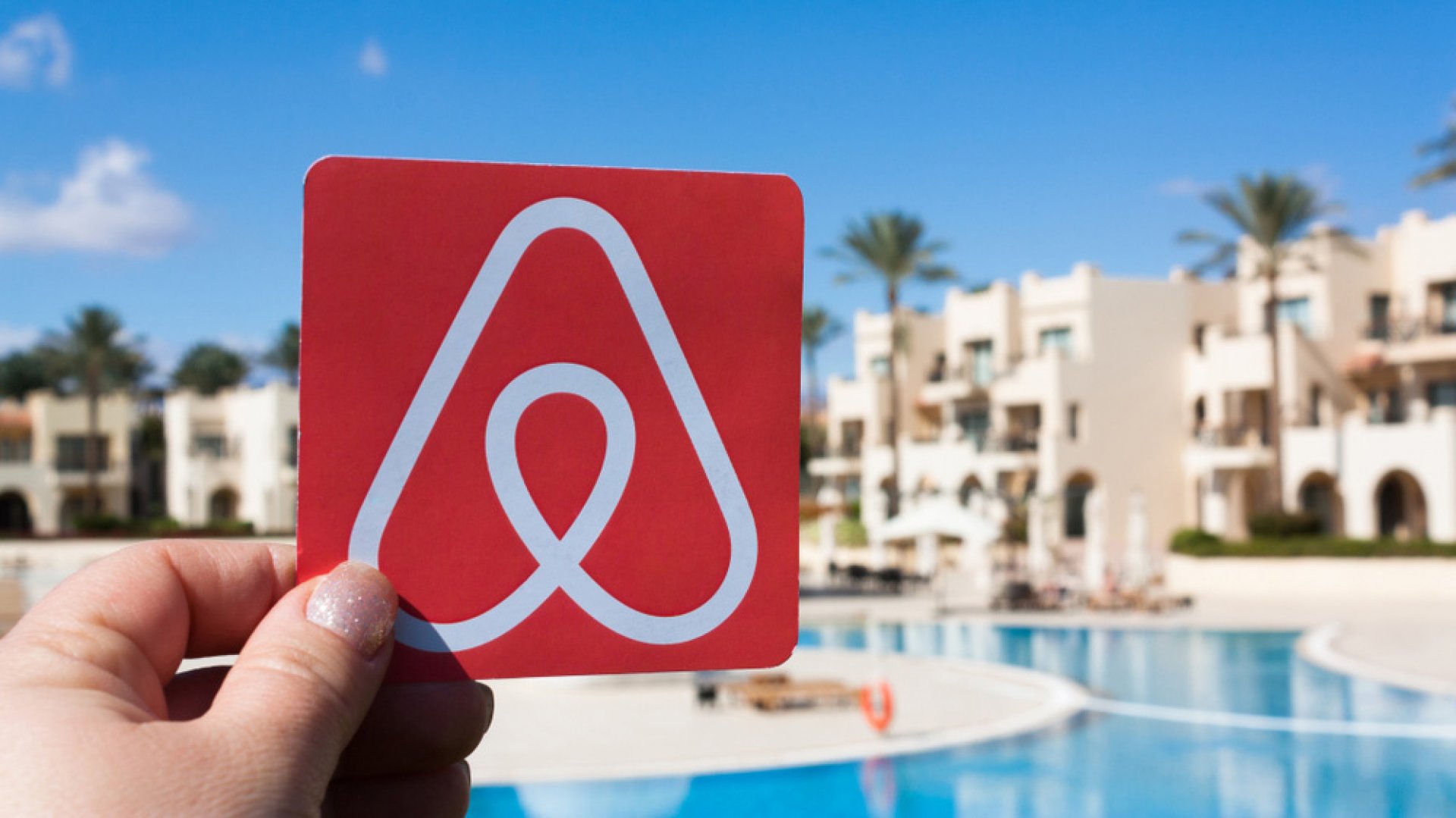 在游泳池前手持 AirBnB 标志的图像